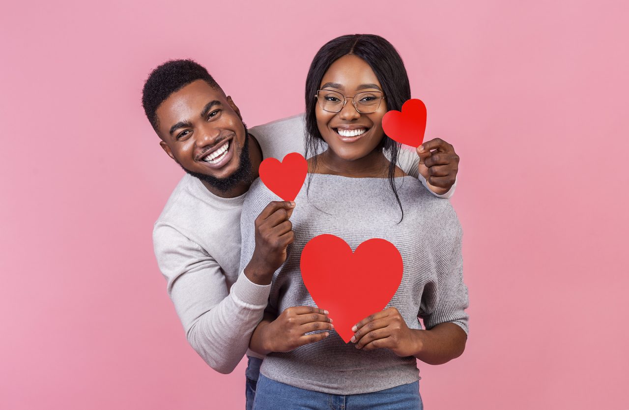 Cheerful afro couple holding red valentines cards