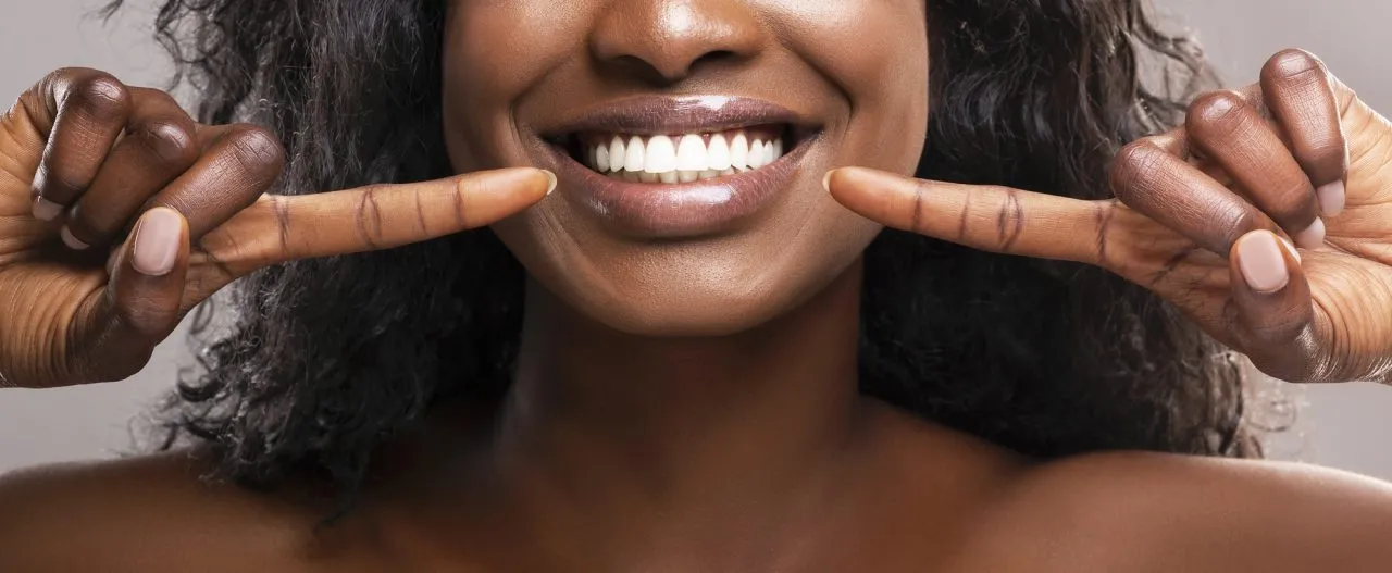 Unrecognizable black woman pointing at her healthy white teeth