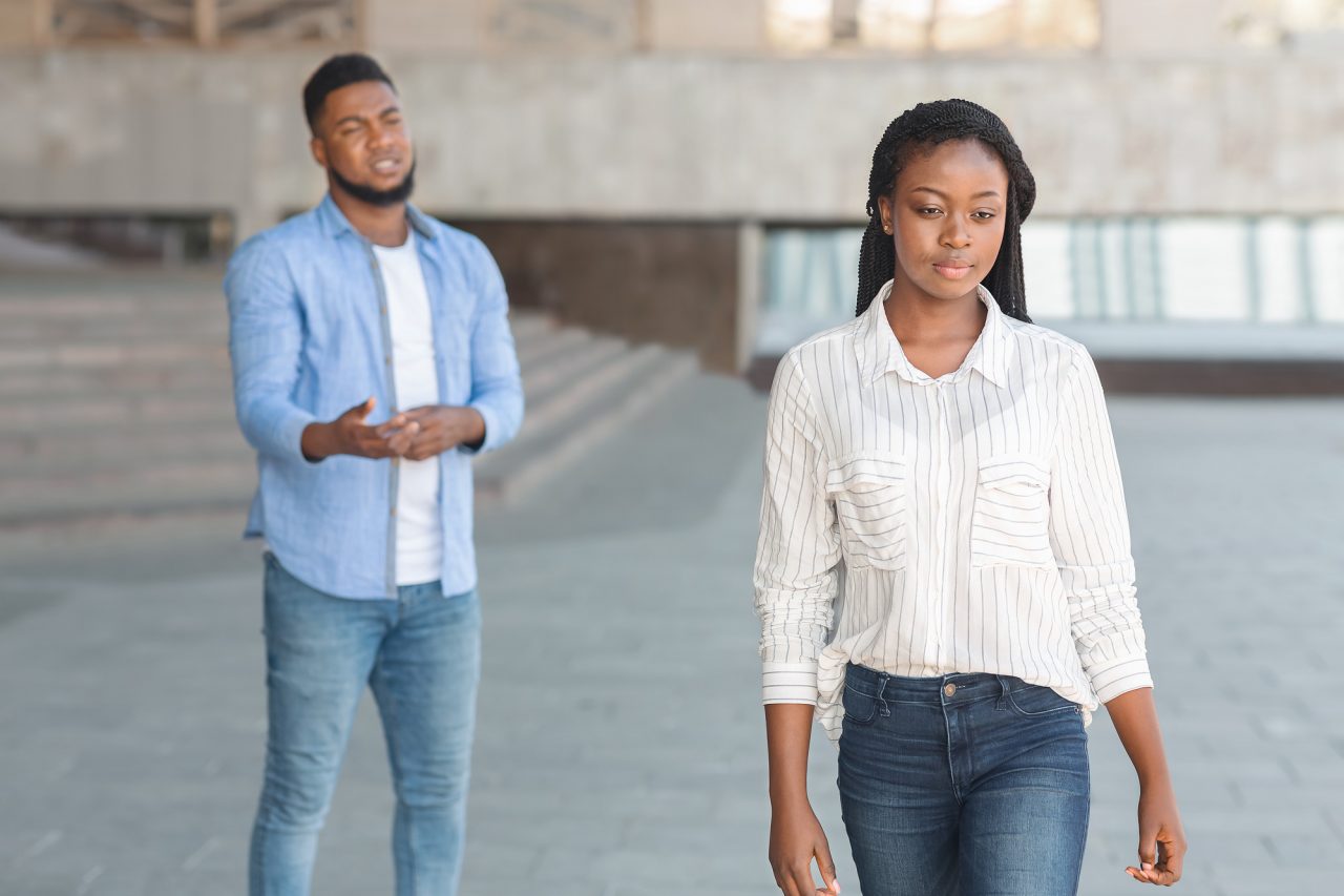 Sad black guy looking at his leaving girlfriend after arguing outdoors